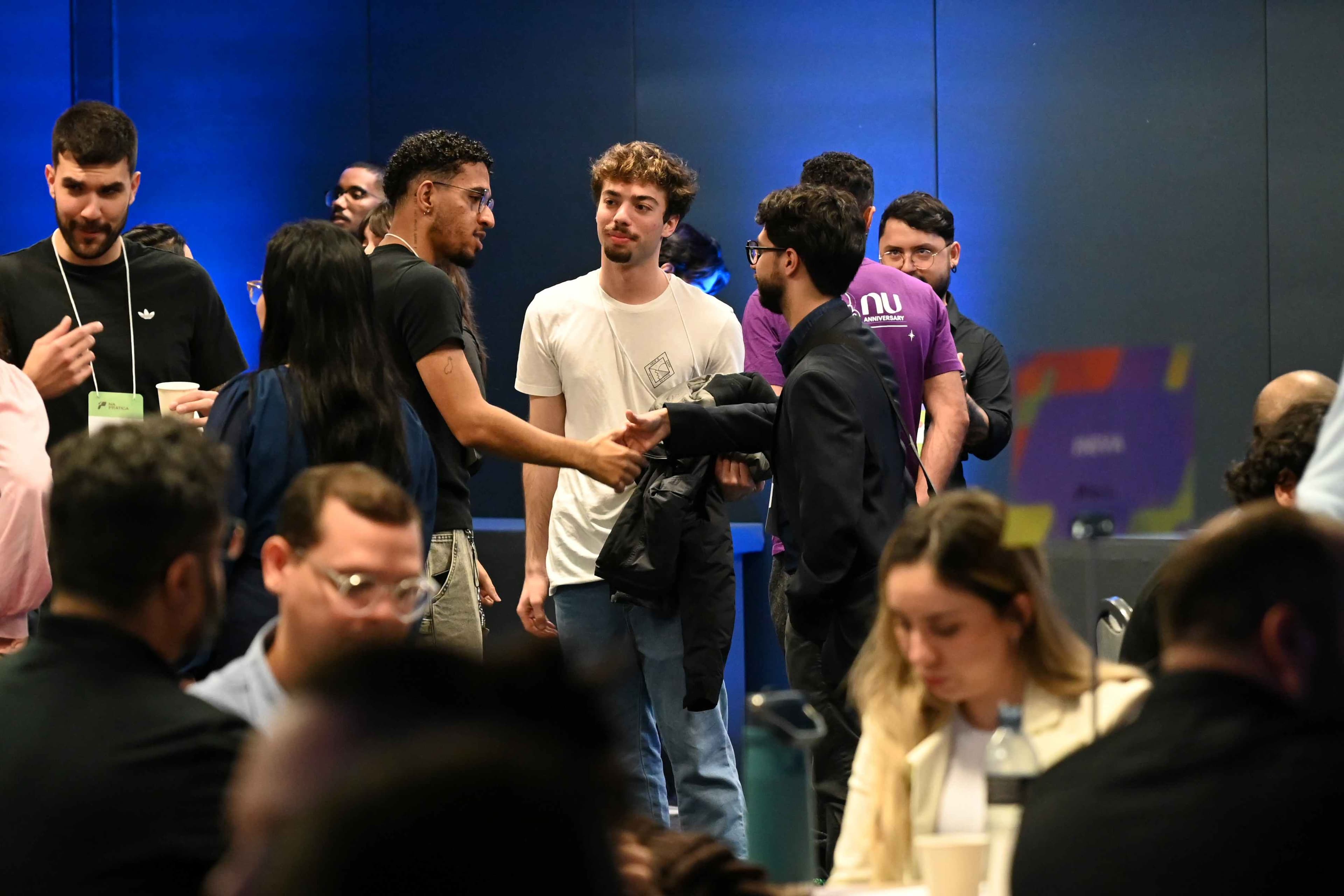 Foto mostra jovem participante da Conferência e representante de uma empresa dando um aperto de mão em meio a outros participantes. 