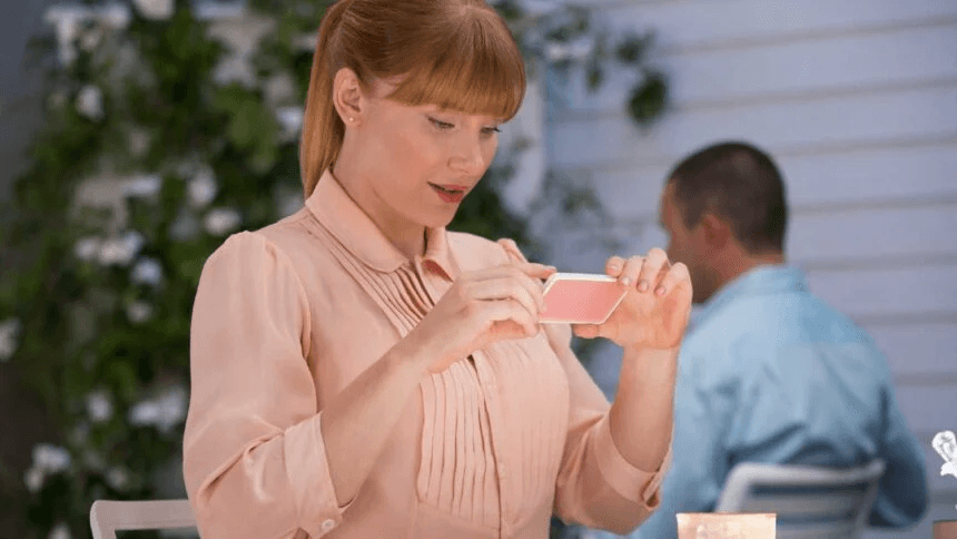 Cena de Black Mirror, com moça ruiva de camisa clara tirando foto da mesa com o celular