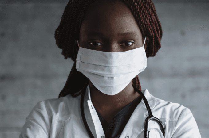 Mulher com máscara veste roupa de médica e tem um estetoscópio