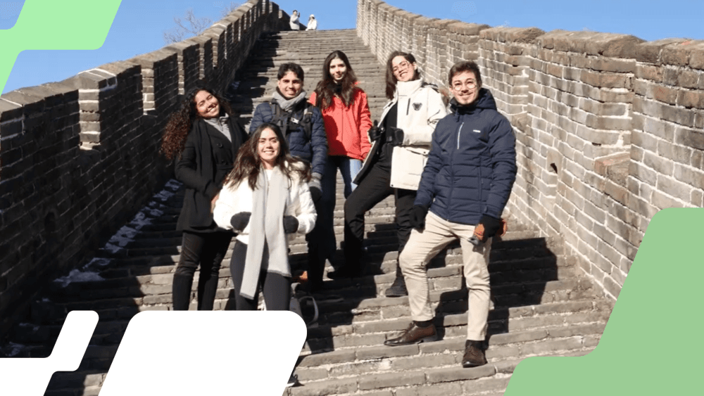 Seis jovens estudantes ganhadores do Prêmio Na Prática protagonismo universitário durante visita á Muralha da China, posando para foto, em um dia ensolarado