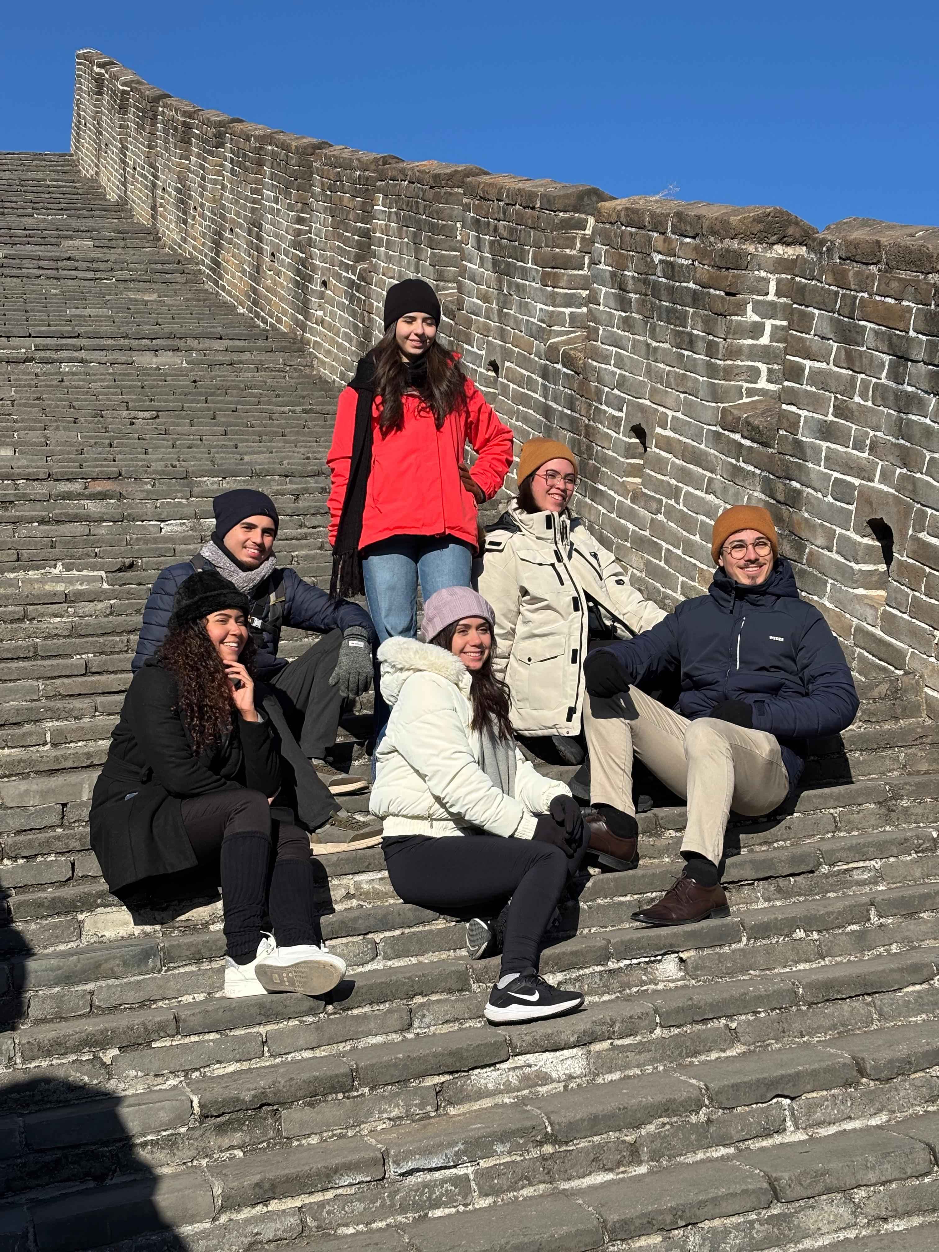 Jovens ganhadores do Prêmio Na Prática Protagonismo Universitário em foto sentados nos degraus da Muralha da China