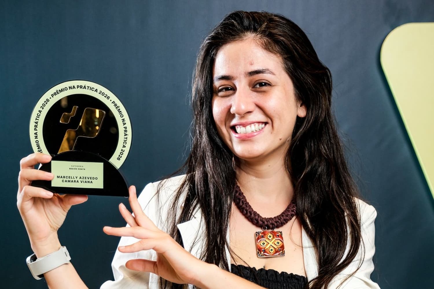 Jovem mulher de cabelo preto comprido, segurando troféu redondo