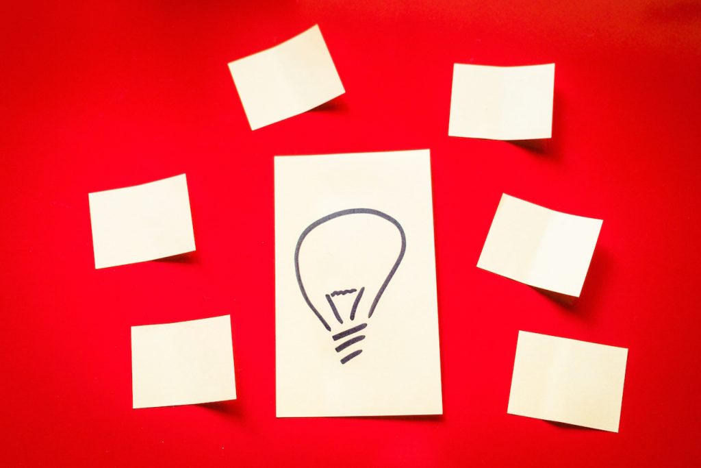 Desenho de uma lâmpada cercado por papeis em brancos sobre mesa vermelha - Descubra tipos de empreendedores