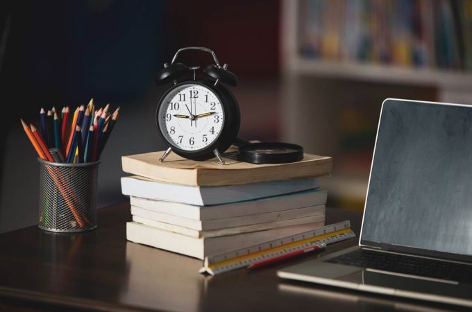 Book,laptop,pencil,clock on wooden table in library,education learning concept