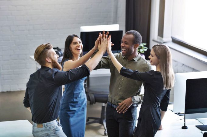 Group of young colleagues giving each other a high five while standing in an office