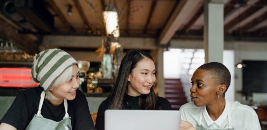 três mulheres em uma mesa olhando a tela do notebook