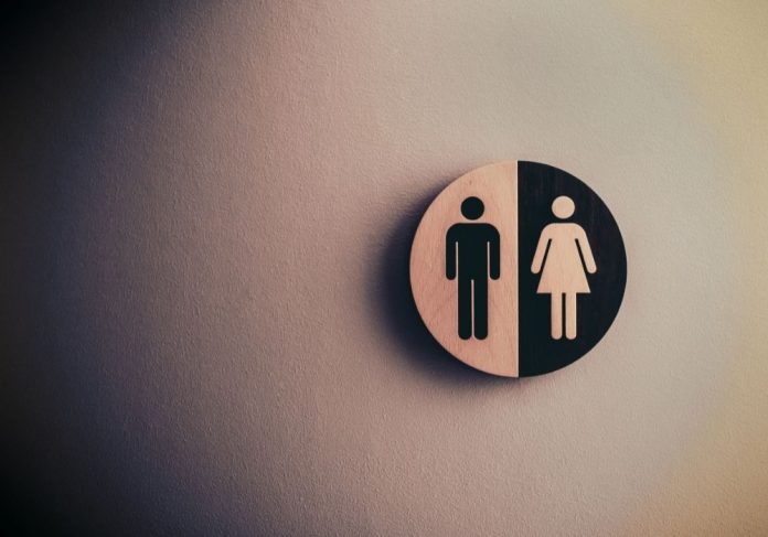 Placa em formato de círculo mostra a imagem da silhueta de um homem e de uma mulher, comum em indicações de gênero em banheiros.