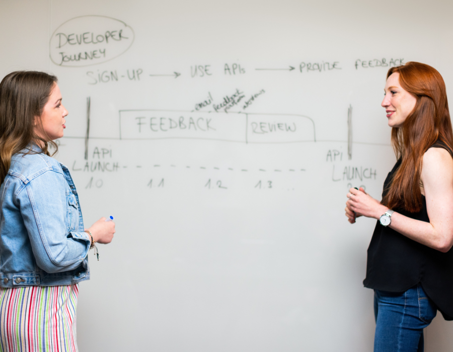 Duas jovens conversam em frente a uma lousa na qual planejam um projeto de intraempreendedorismo