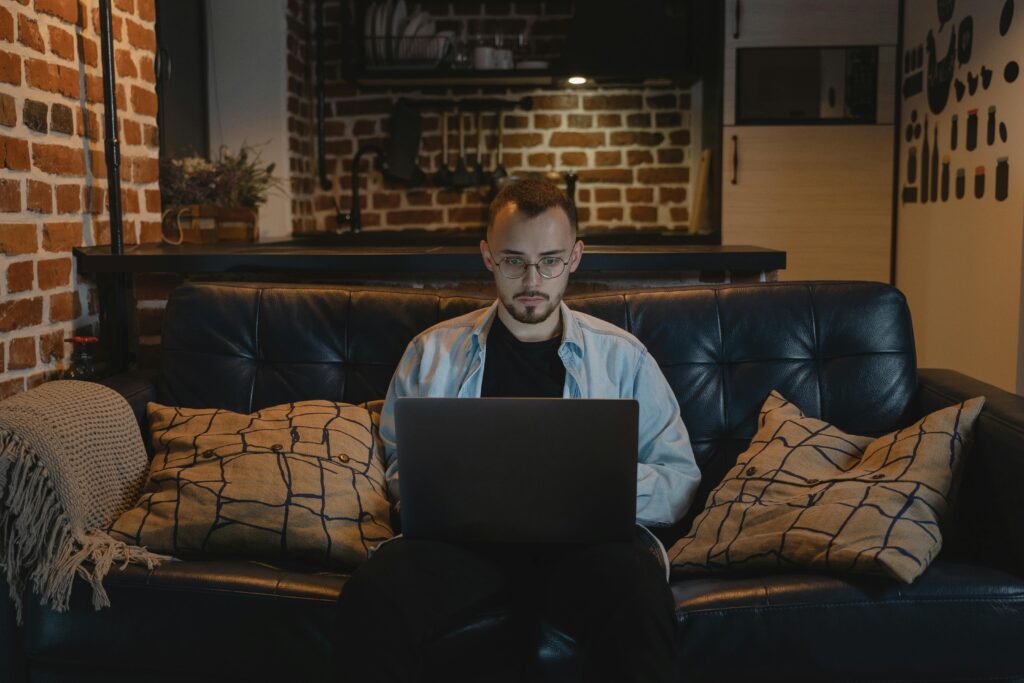 Profissional que atua com trabalho híbrido em seu dia de home office, em sua sala, no sofá, com o notebook no colo.