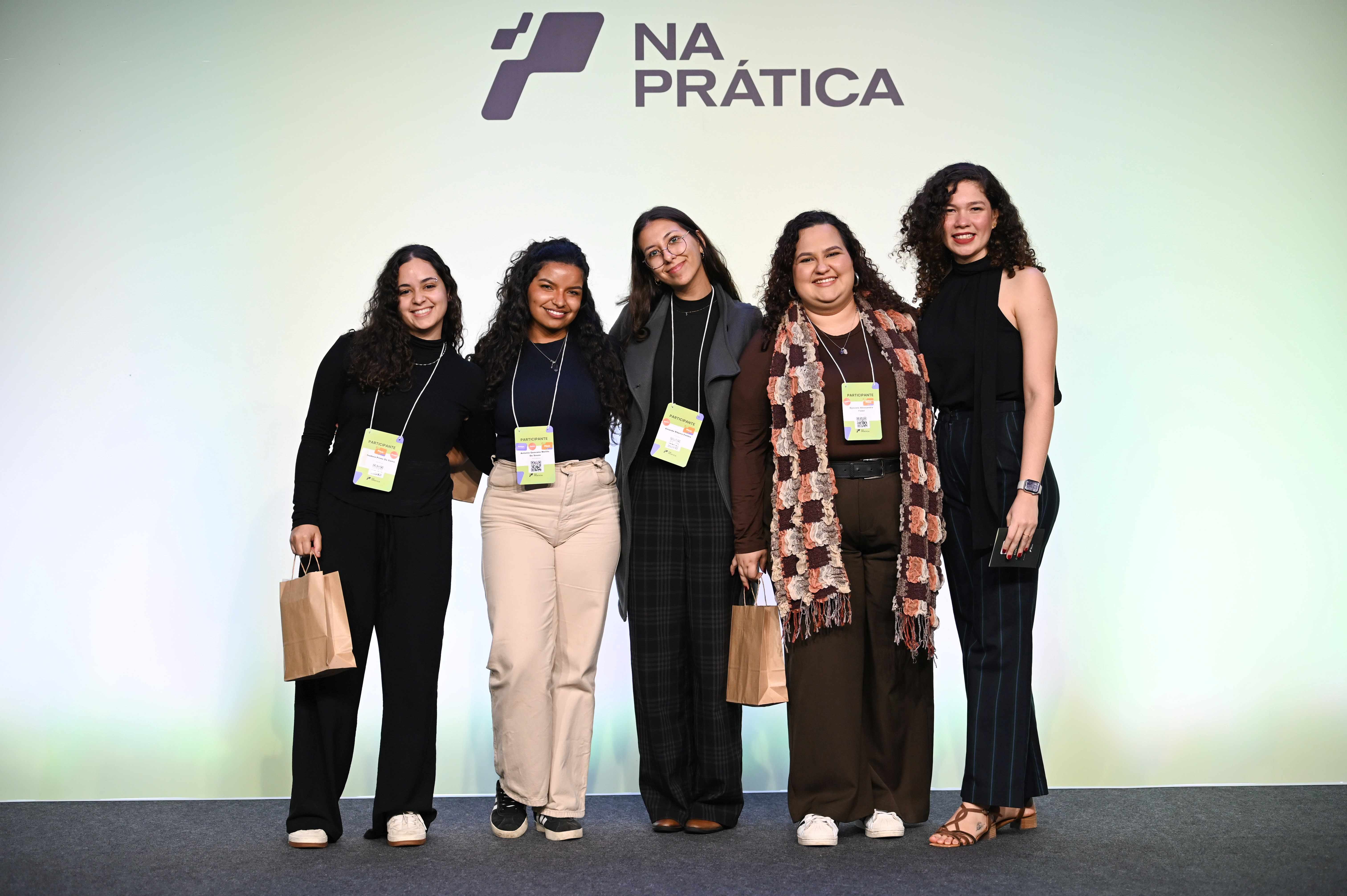 A foto mostra quatro jovens, vencedoras dos pitches premiados da Conferência Na Prática, ao lado de Lorena Santos, mulher branca, alta, de cabelos cacheados e vestindo preto, que é a curadora do evento.